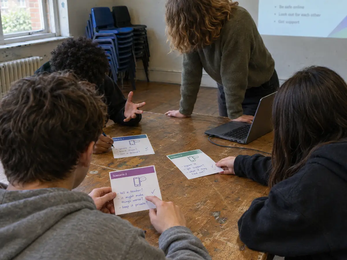 Young people compare handwritten scenario cards around a table while a facilitator listens.