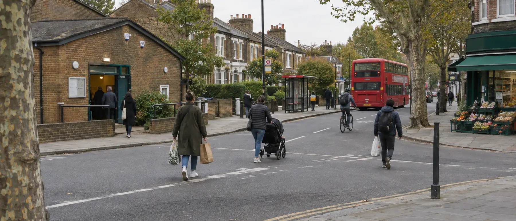 An ordinary London street: a community hall, a bus stop, people crossing with shopping and a pushchair.