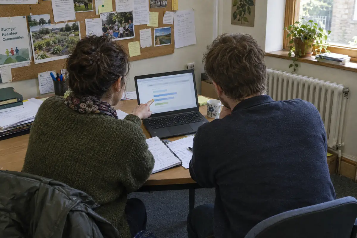 Two practitioners talk through an angled data view on a laptop in a community office.
